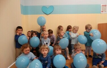 Sala zabaw-grupa dzieci siedzi na dywanie. W ręce trzymają niebieskie balony.