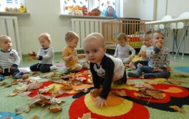 Sala zabaw-na dywanie leżą jesienne liście i siedzi grupka dzieci. 