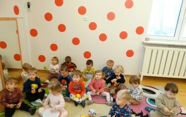 Grupka dzieci siedzi na dywanie, w ręce trzyma małe instrumenty muzyczne.