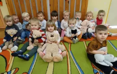 Na podłodze siedzą dzieci i trzymają maskotki misie.