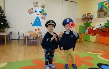 Na kolorowym dywanie stoją chłopcy w przebraniu policjanta. Jeden z nich ma w rączce znak z białym napisem STOP.