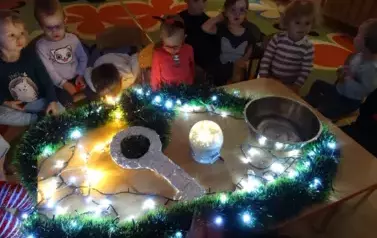 Przy stoliku siedzą dzieci a na nim stoi miska, świecąca kula  i duży klucz.