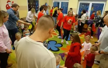 Grupa dorosłych os&oacute;b z dziećmi stoi na dywanie, w tle świąteczne dekoracje.