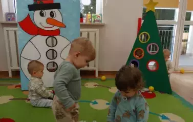 Dzieci stoją na dywanie, w tle choinka i mikołaj.