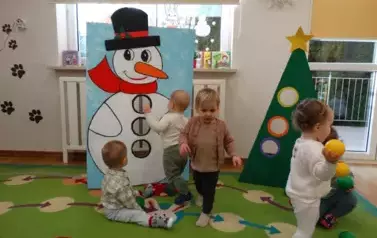 Dzieci stoją na dywanie, w tle choinka i mikołaj.