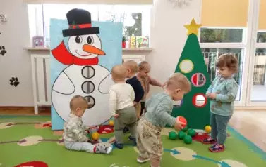 Grupka dzieci stoi na dywanie, w tle choinka i mikołaj.