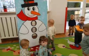 Dzieci stoją na dywanie, w tle olbrzymi mikołaj.