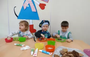 Przy stoliku siedzą dzieci. Rączkami dotykają zawartości talerzyka.