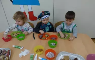 Przy stoliku siedzą dzieci. Rączkami dotykają zawartości talerzyka.