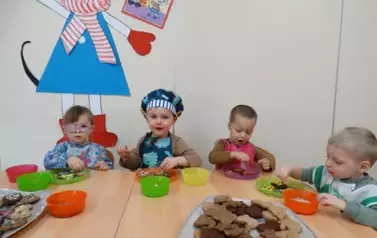 Przy stoliku siedzą dzieci. Rączkami dotykają zawartości talerzyka.