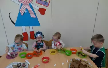 Przy stoliku siedzą dzieci. W ręce trzymają kolorowe tubki.