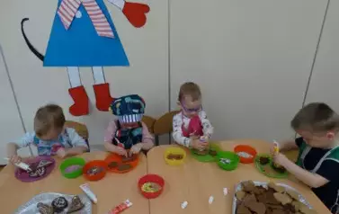 Przy stoliku siedzą dzieci. W ręce trzymają kolorowe tubki.