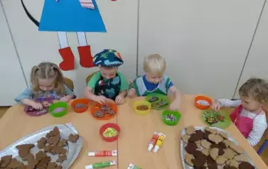 Przy stoliku siedzą dzieci. Rączkami dotykają zawartości talerzyka.