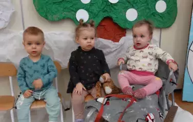 w-dw&oacute;jka dzieci siedzi na krzesełkach, trzecie dziecko na sankach.