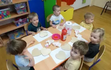 Sala zabaw-grupka dzieci siedzi przy stoliku, na kt&oacute;rym leżą jasne serduszka.
