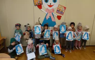 Sala zabaw-grupka dzieci w czapkach na głowach trzyma w ręce obrazek bałwana. W tle Kicia Kocia z książeczką w ręce.