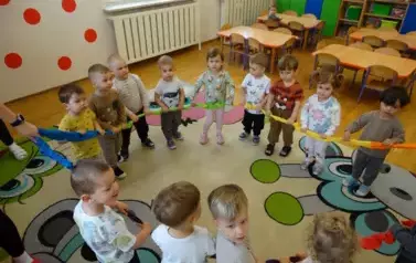 Grupa dzieci stoi na kolorowym dywanie przy wężu spacerowym. 