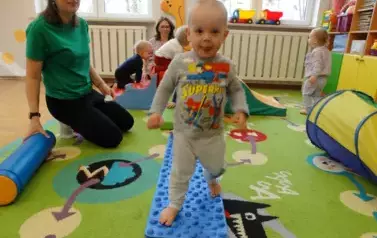 Sala zabaw-na dywanie leży niebiesko-szary dywanik, po kt&oacute;rych chodzą dzieci.