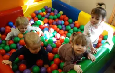 Basen z kolorowymi piłkami a w nim grupka dzieci.