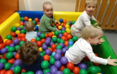 Basen z kolorowymi piłkami a w nim grupka dzieci.