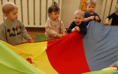 Sala zabaw-grupka dzieci trzyma w ręce kolorową chustę animacyjną.