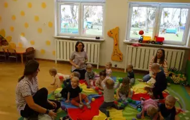 Sala zabaw-na dywanie leży kolorowa chusta animacyjna a na niej siedzą dzieci.