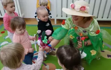Sala zabaw-kolorowa Pani Wiosna trzyma w ręce kwiaty. Tuż obok niej stoją dzieci z kwiatami.dzieci 