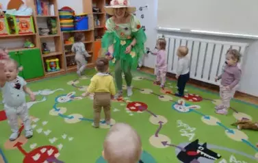 Sala zabaw-Pani Wiosna z grupką dzieci stoi na dywanie. 