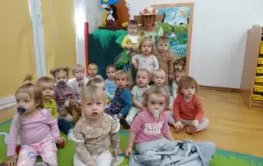 Sala zabaw-Pani Wiosna z dzieckiem na kolanach siedzi na krześle. Tuż przed nią na dywanie siedzi grupka dzieci. 