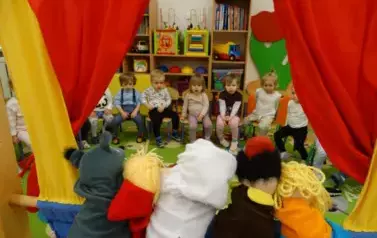 Sala zabaw-na pierwszym planie kolorowe pacynki. W tle dzieci siedzące na krzesełkach.