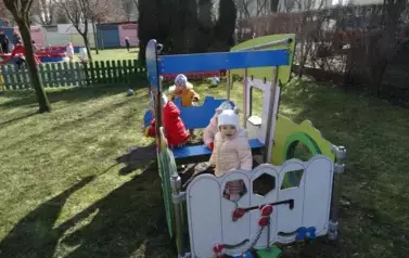 Plac zabaw-grupka dzieci w kolorowych czapkach i kurtkach siedzi w wagoniku.