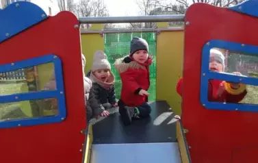 Plac zabaw-grupka dzieci w kolorowych czapkach i kurtkach siedzi na zjeżdżalni.