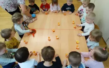 Sala zabaw-dzieci siedzą przy stoliku, na kt&oacute;rym stoją ż&oacute;łte kurczaczki i pojemniki z ziarenkami.