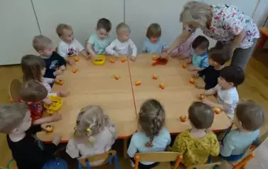 Sala zabaw-dzieci siedzą przy stoliku, na kt&oacute;rym stoją ż&oacute;łte kurczaczki i pojemniki z ziarenkami.