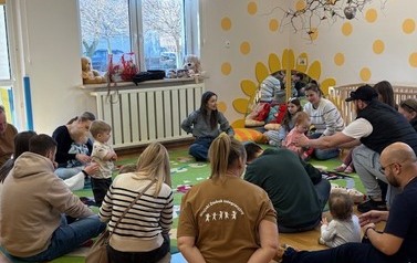 Sala zabaw-na kolorowym dywanie siedzi grupka dorosłych z dziećmi.