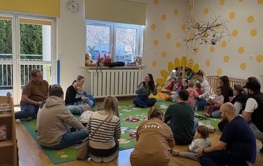 Sala zabaw-na kolorowym dywanie siedzi grupka dorosłych z dziećmi.