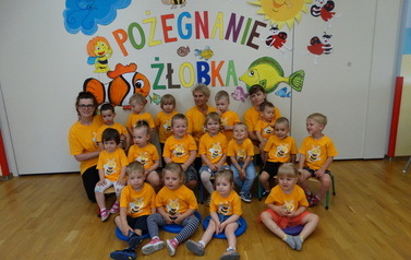 Grupa dzieci z opiekunami, w tle kolorowy napis "Pożegnanie żłobka"