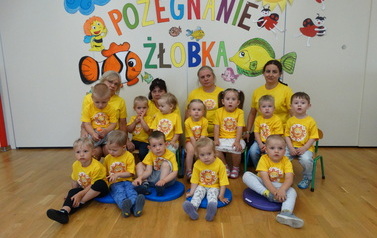 Grupa dzieci z opiekunami, w tle kolorowy napis "Pożegnanie żłobka"