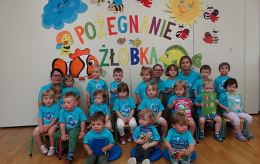 Grupa dzieci z opiekunami, w tle kolorowy napis "Pożegnanie żłobka"