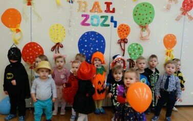 Sala zabaw-na pierwszym planie grupka dzieci w strojach postaci z bajek. W tle kolorowe balony i napis "BAL 2024"