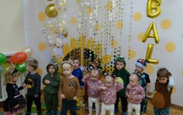 Sala zabaw-na tle jasnej ściany z napisem "BAL" stoi grupa dzieci w strojach postaci z bajek.     