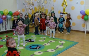 Sala zabaw-na pierwszym planie dziewczynka w stroju biedronki. W oddali stoi grupa dzieci na tle jasnej ściany z napisem "BAL".