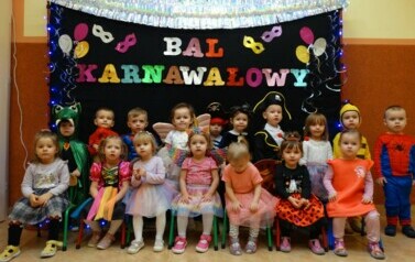 Na tle czarnej ścianki z kolorowym napisem "Bal Karnawałowy" grupa dzieci w strojach postaci z bajek. 