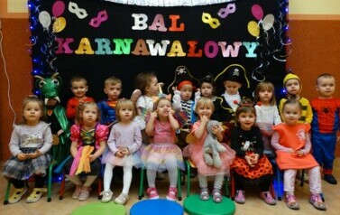 Na tle czarnej ścianki z kolorowym napisem "Bal Karnawałowy" grupa dzieci w strojach postaci z bajek. 