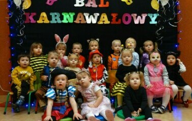 Na tle czarnej ścianki z kolorowym napisem "Bal Karnawałowy" grupa dzieci w strojach postaci z bajek. 