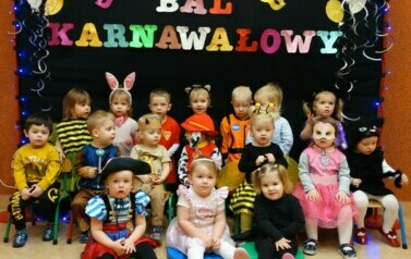 Na tle czarnej ścianki z kolorowym napisem "Bal Karnawałowy" grupa dzieci w strojach postaci z bajek. 