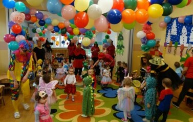 Sala zabaw-opiekunowie z grupą dzieci w strojach postaci z bajek. W tle kolorowe balony.