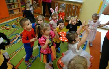 Sala zabaw-grupa dzieci w strojach postaci z bajek wyciąga rączki w kierunku mydlanych baniek..