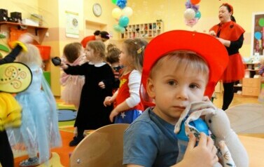 Sala zabaw-na pierwszym planie chłopiec w czerwonej czapce z daszkiem tuli do siebie pluszaka. W tle grupka bawiących się dzieci.