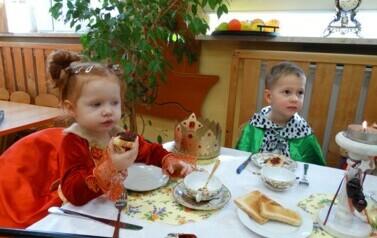 Sala zabaw-przy stole siedzi dziewczynka z chłopcem w kr&oacute;lewskich strojach. Dziewczynka w stroju kr&oacute;lowej trzyma w ręce tosta. Tuż obok niej leży korona i berło. 